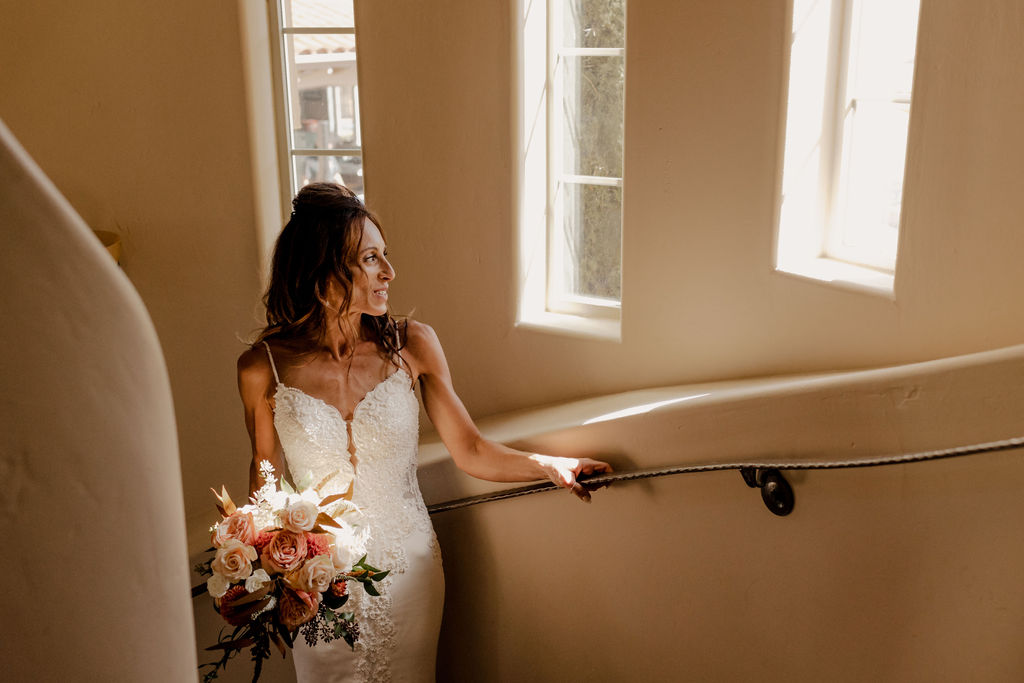 bride standing on stairs looking out at window during bridal photos