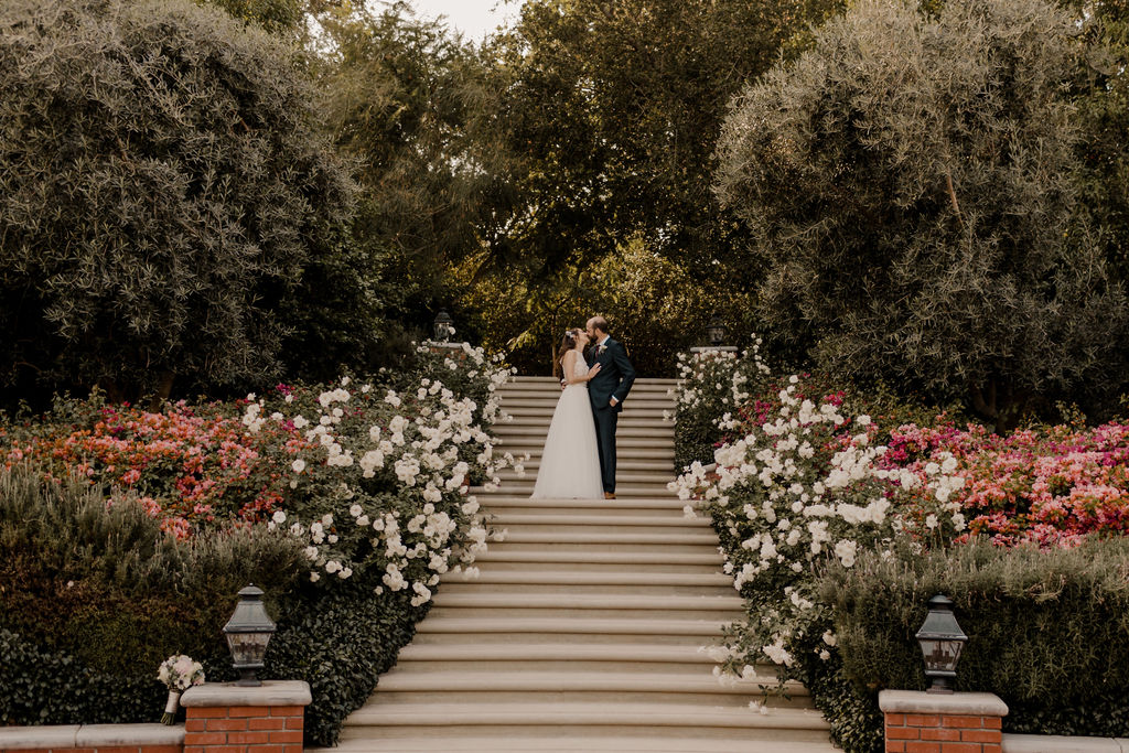bride and groom kissing on top of stairs during their outdoor wedding