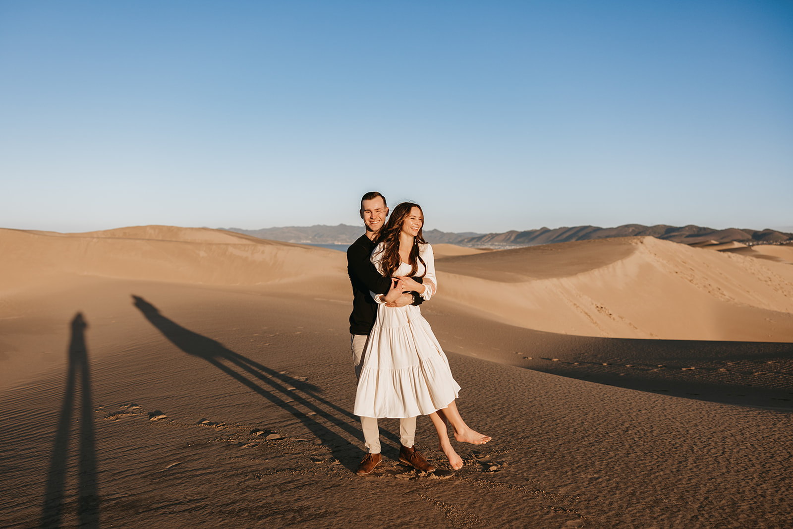 couple playing in sand dunes taking their engagement photos