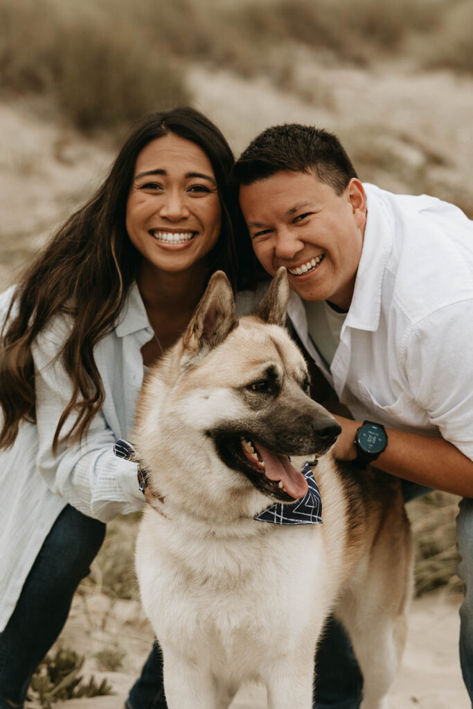 couple posing with their dog on a beach for their moody engagement photoshoot | Moody Engagement Photos at Montana de Oro State Park
