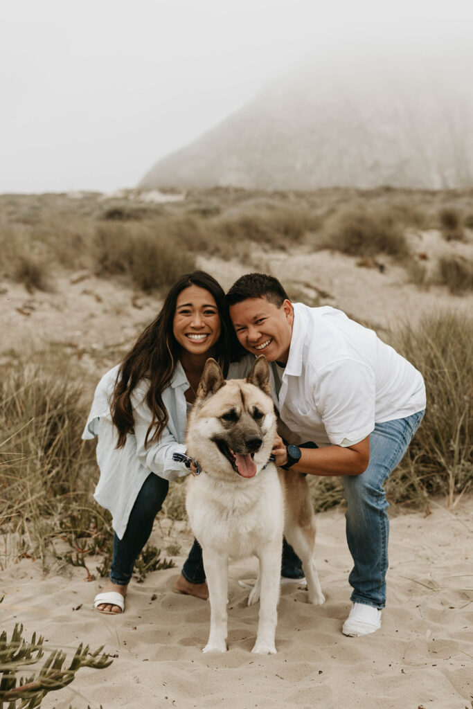 couple posing with their dog on a beach for their moody engagement photos
