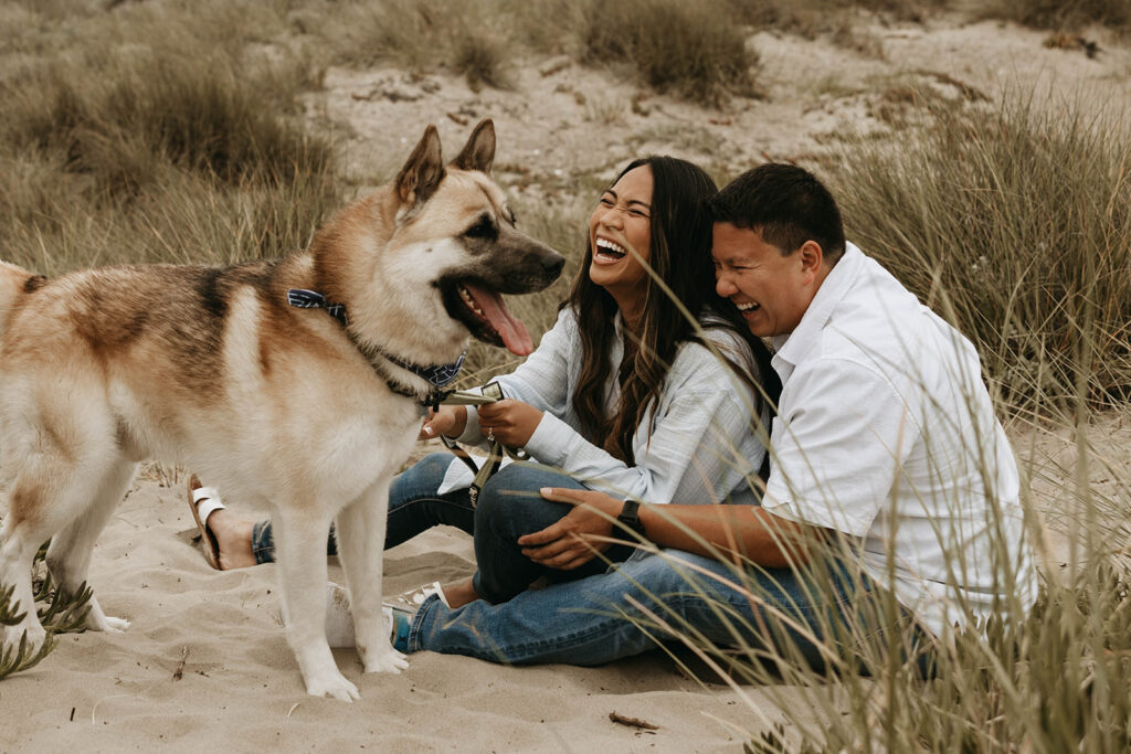 couple posing with their dog on a beach for their moody engagement photoshoot
