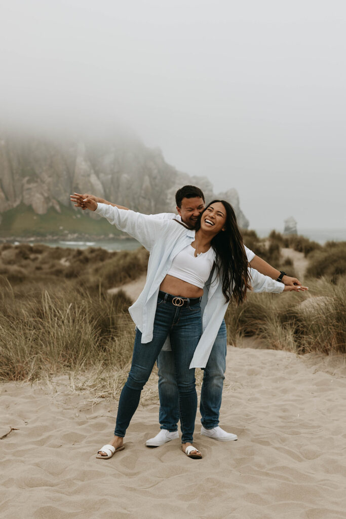 playful couple posing on a beach in California for a moody engagement photoshoot
