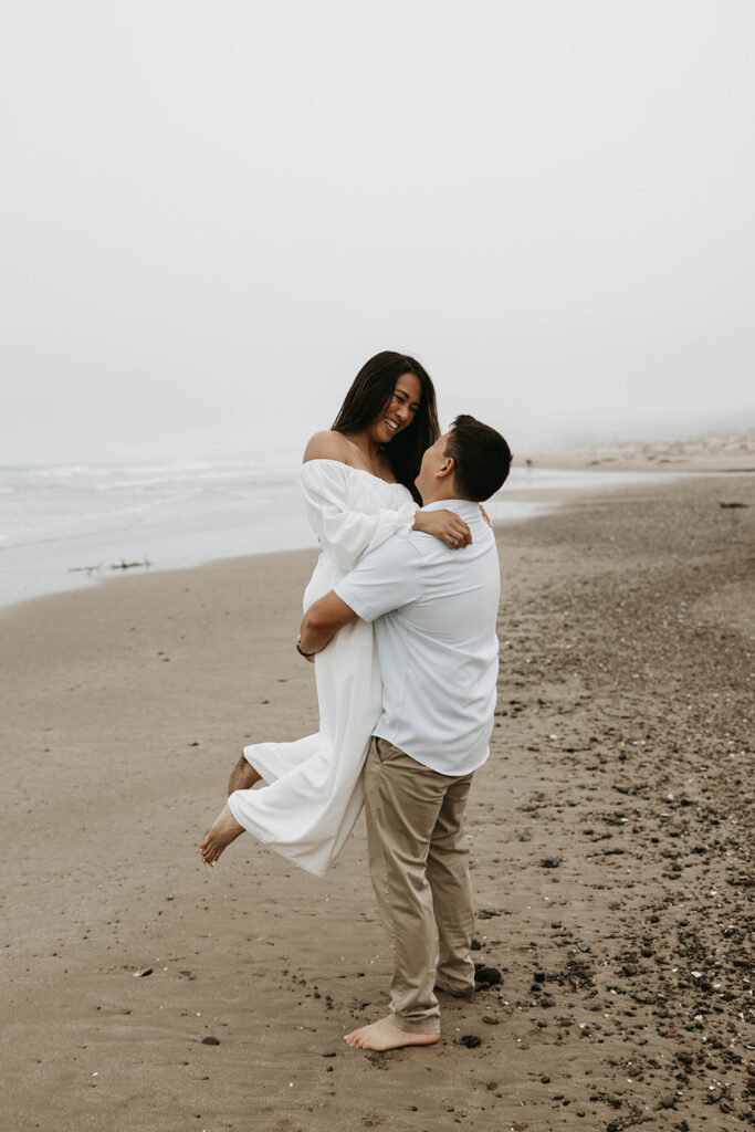 a couple running around on the beach posing for their moody engagement photoshoot
