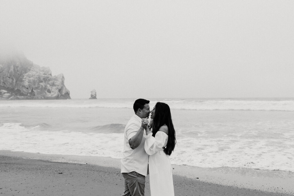a couple posing for a romantic moody photoshoot on the beach to celebrate their engagement
