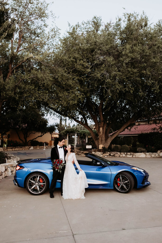 bride and groom posing by a blue car for their wedding portraits