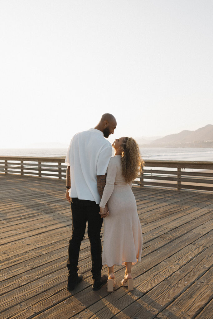 couple posing near pismo beach sand dunes and the pier for their engagement photos
